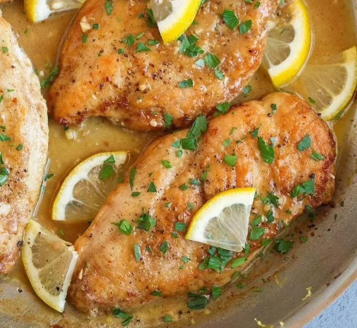 Plate of flavorful lemon chicken garnished with herbs and lemon slices
