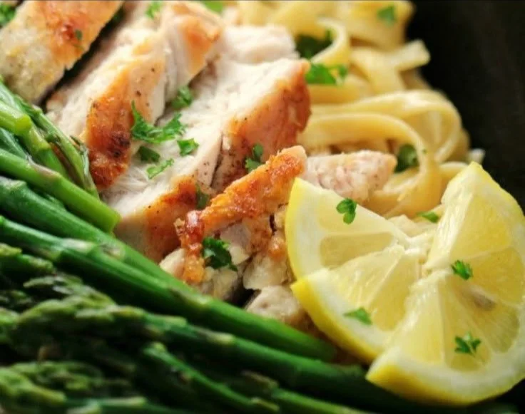 Plate of lemon chicken and asparagus pasta garnished with fresh herbs